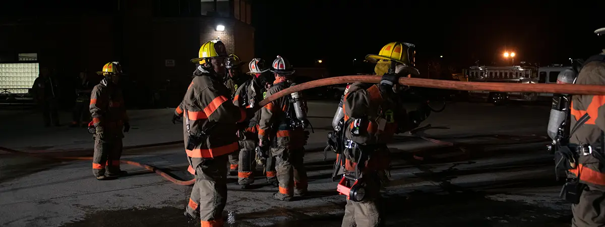 Firefighters carrying a hose at night